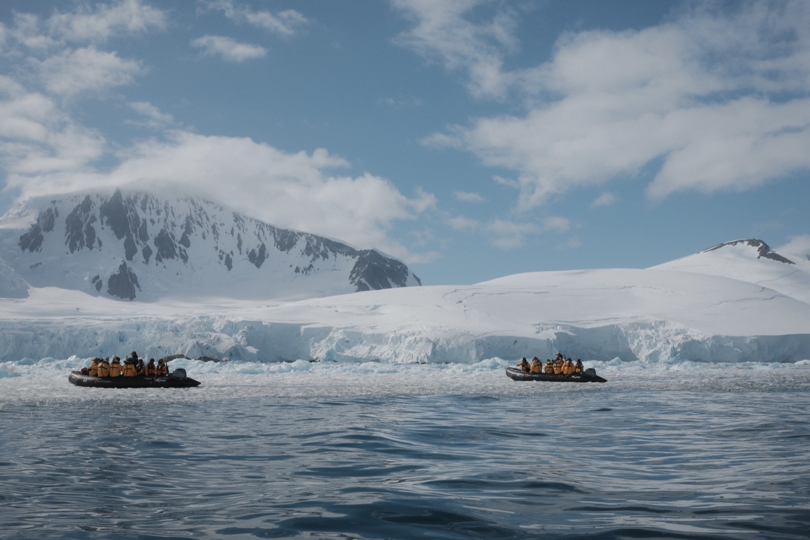 Two Zodiacs of travellers in expedition parkas working along a glacier face on the Antarctic Peninsula