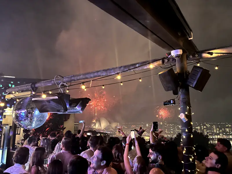 A rooftop party at night, lights strung overhead and the city behind.