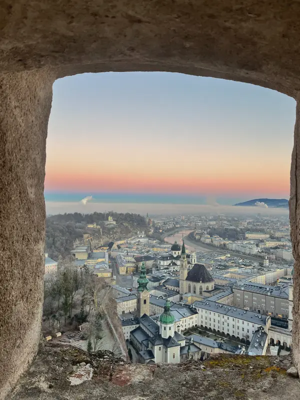 Salzburg through a stone arch at dusk, the old town laid out below.