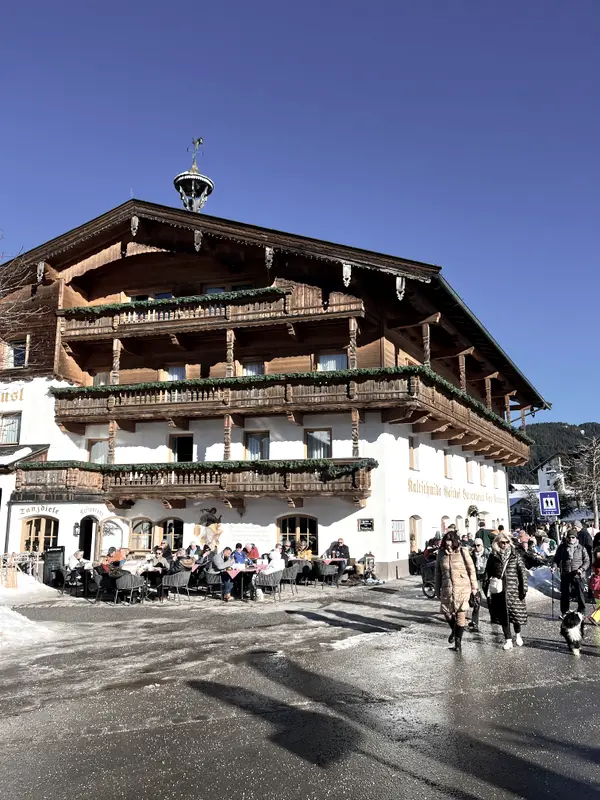 A large wooden chalet on the village street, people out in front of it.