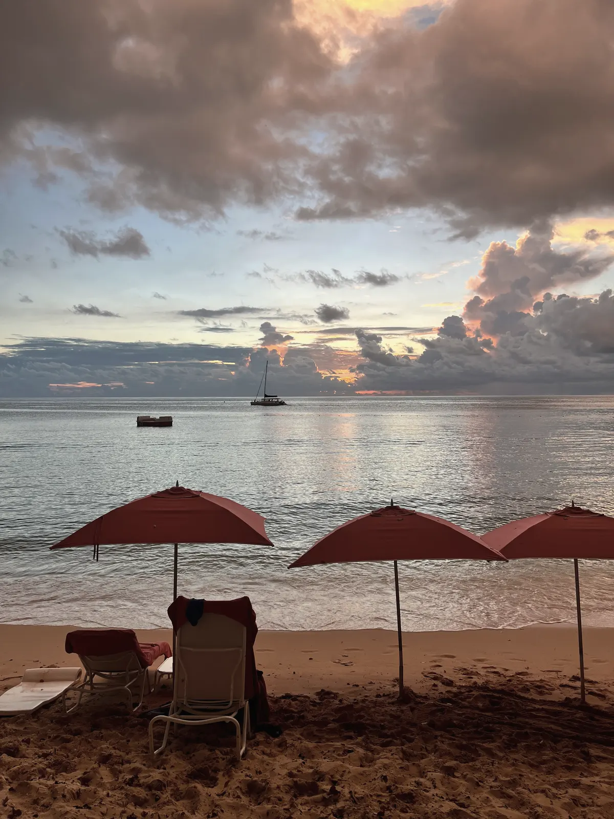 Red umbrellas on the sand at sunset, a boat anchored offshore.