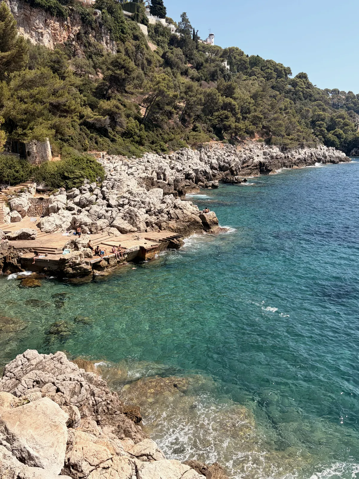 A rocky cove on the Côte d'Azur, water clear enough to read the bottom.