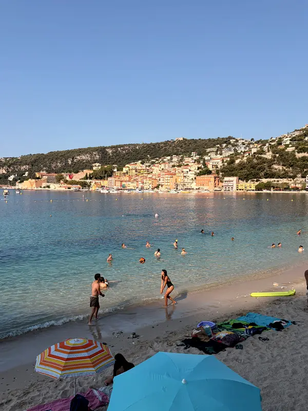 The beach at Villefranche, umbrellas up and the village stacked on the hill behind.