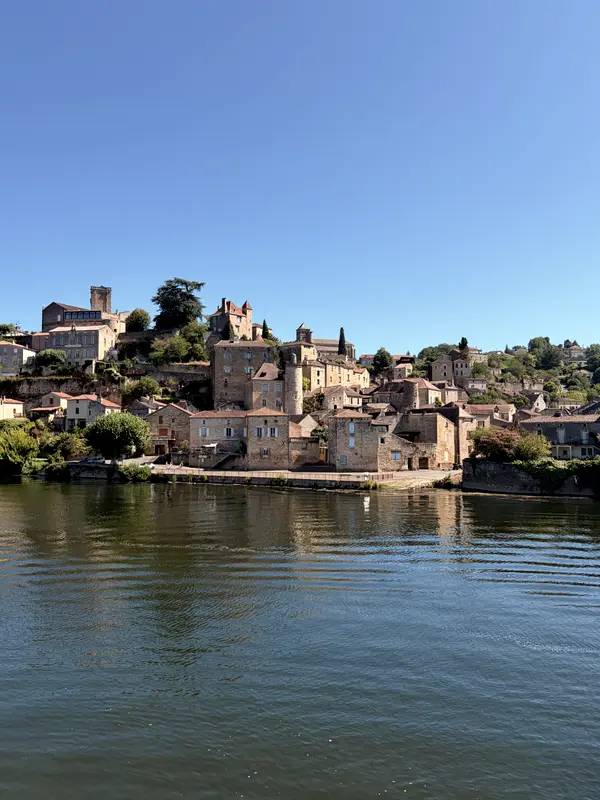 A hilltop village above the river in the Lot, reflected in still water.