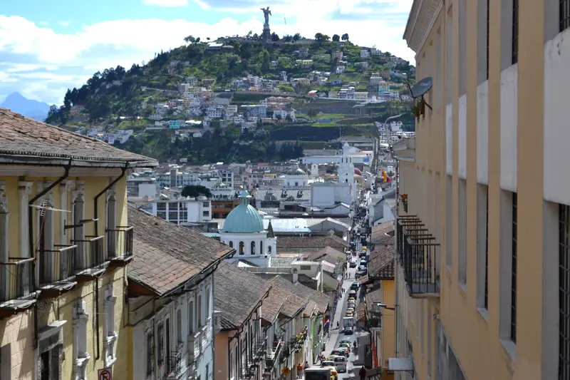 Quito rooftops falling away down a colonial street, the Virgen del Panecillo on the hill above the city.