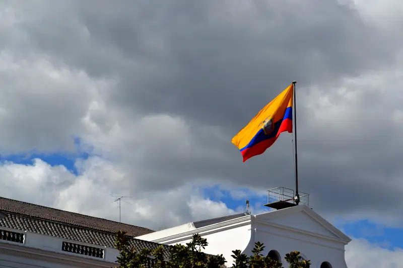 The Ecuadorian flag flying over the Presidential Palace in Quito under heavy cloud.