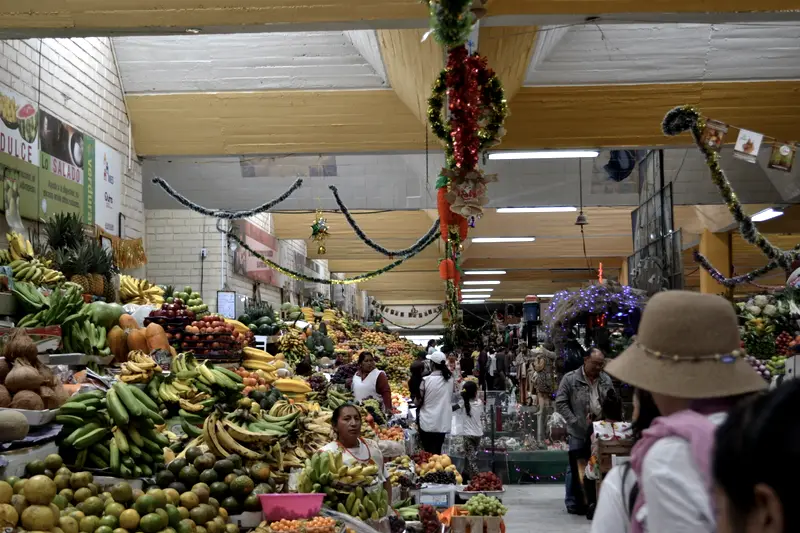 A covered market in Quito at Christmas, fruit stalls stacked high under tinsel and garlands.