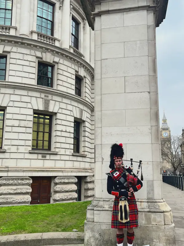 A piper in full dress playing beside a stone column in Whitehall.