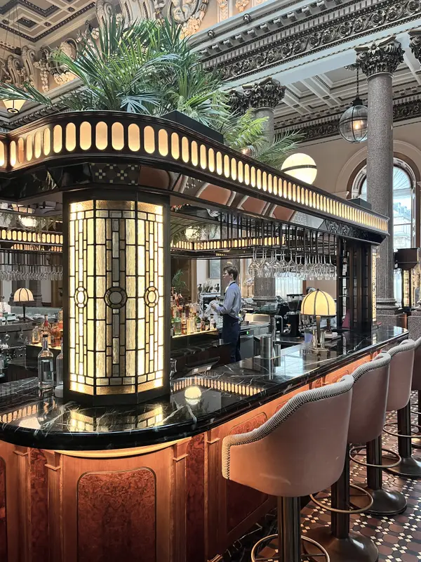 A hotel bar under a stained-glass canopy, brass and low light.