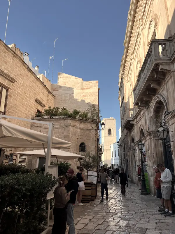 A street in a Puglian town, stone buildings and awnings out over the tables.
