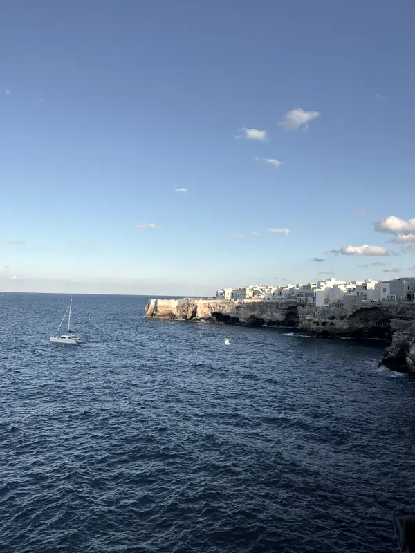 The coast at Polignano at dusk, a sailboat off the cliffs.