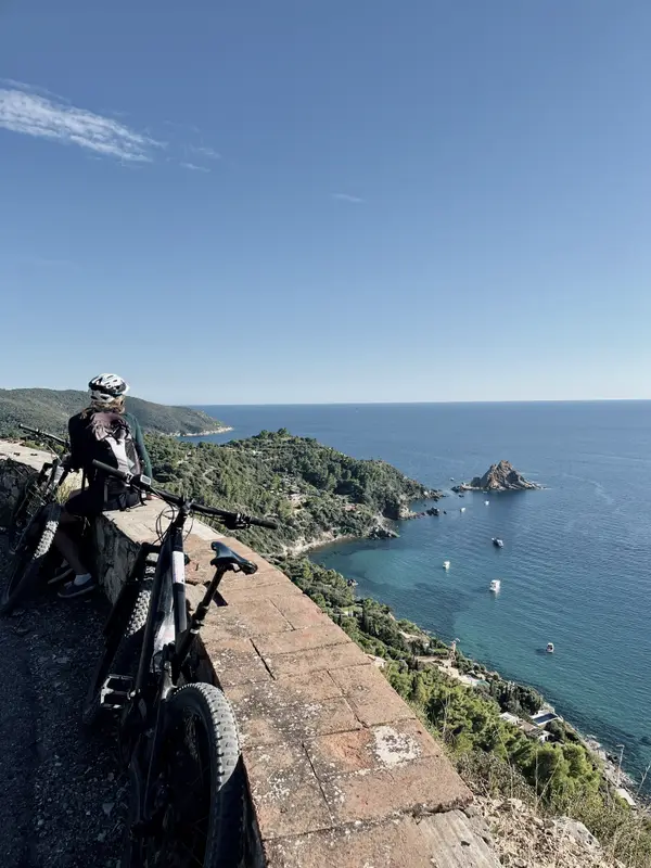 An e-bike propped on a terrace above the coast, headland and islet beyond.