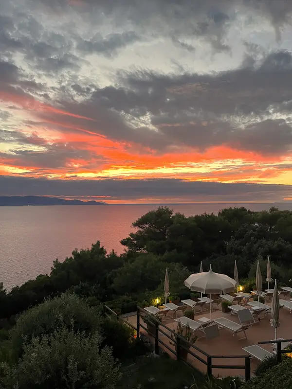 A hard red sunset over the water, tables laid on the terrace below.