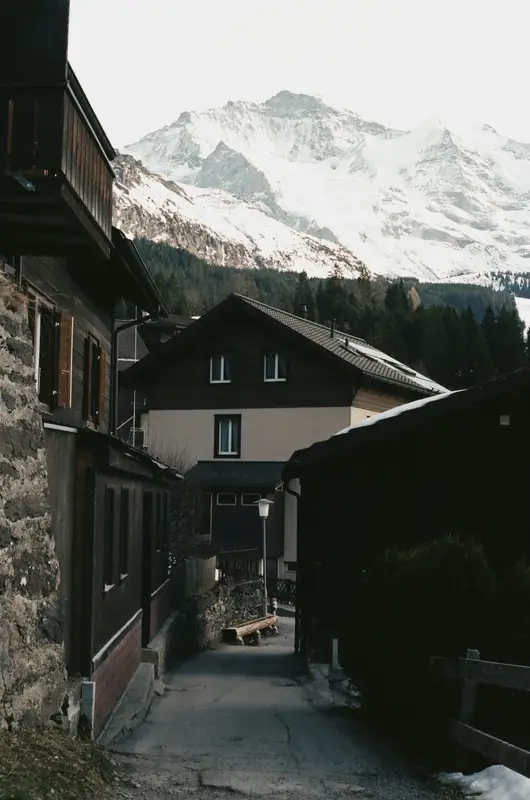 A lane in Wengen on 35mm, chalet eaves on both sides and the snow massif filling the gap above.