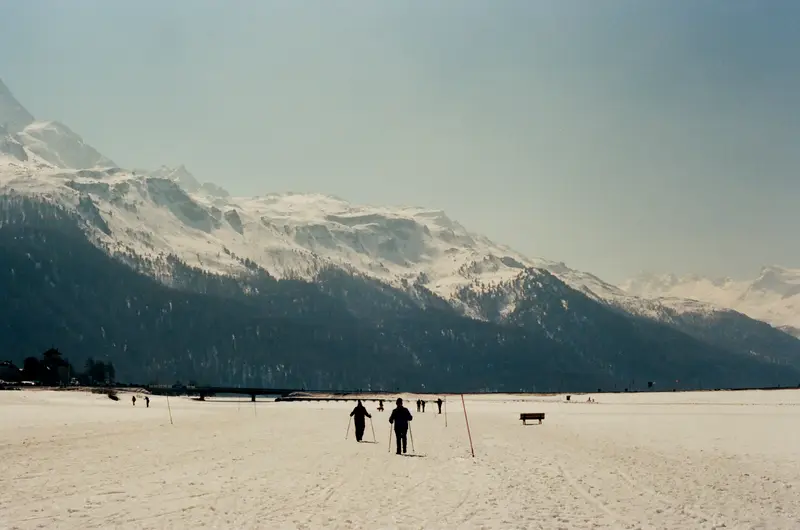 The frozen lake at St. Moritz on film, two figures walking out across it.