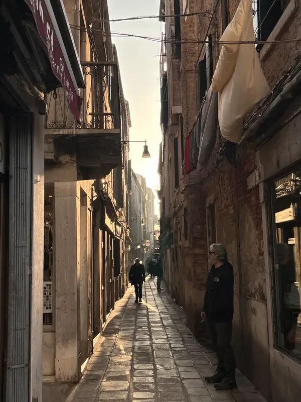 A Venice back lane at dusk, awnings out and two figures at the far end.
