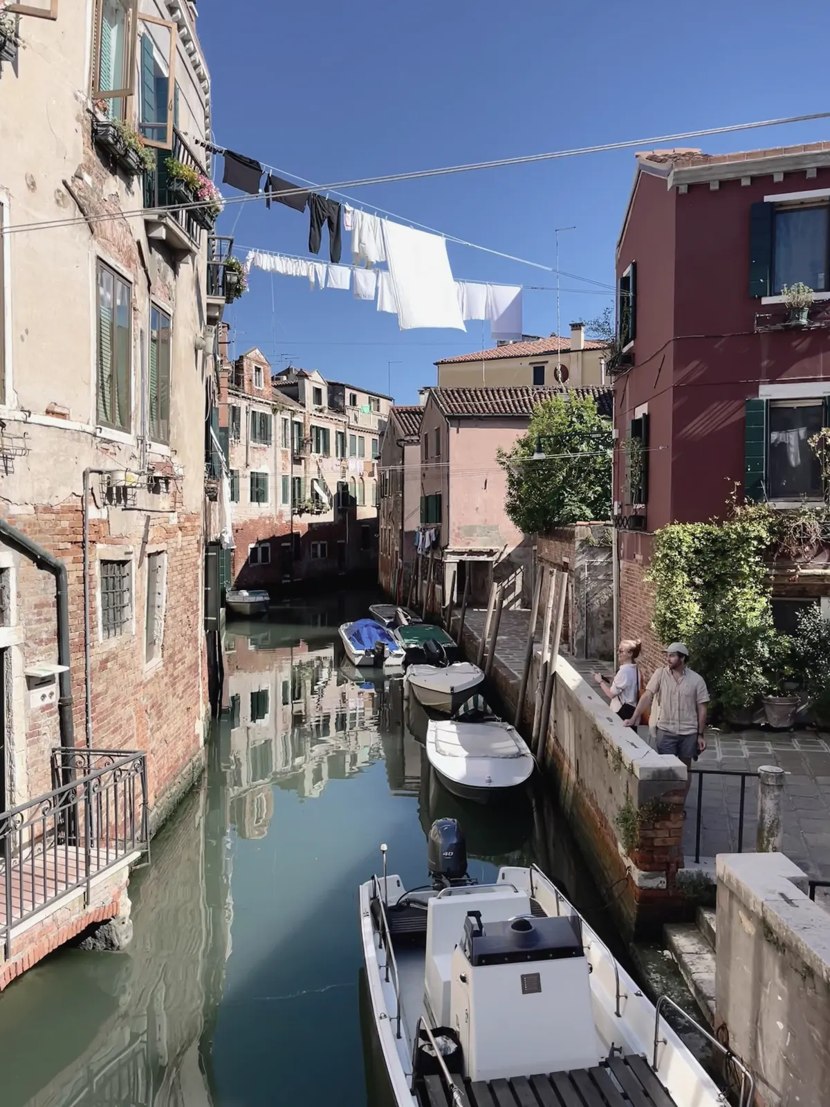 A quiet Venice canal, washing strung between the houses and boats tied along the wall.