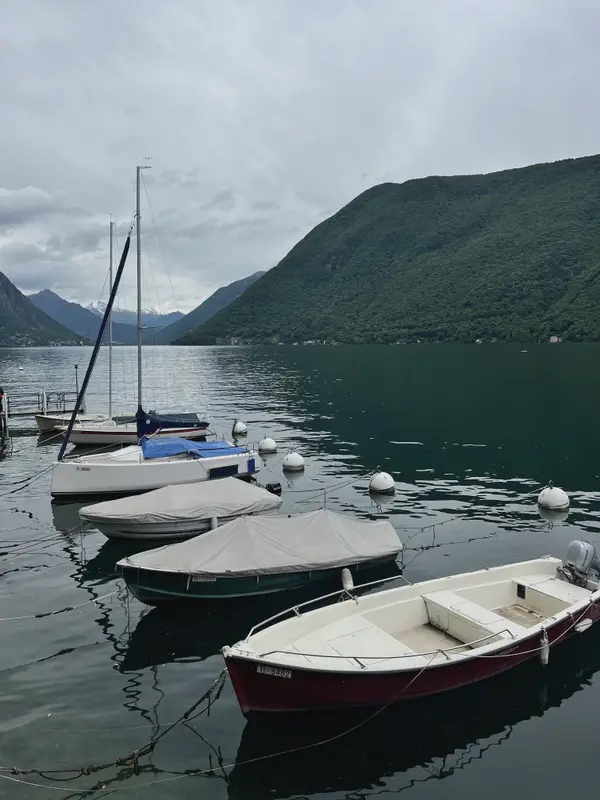Small boats moored in flat water under a steep green shore.