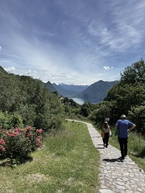 A path above the lake with oleander in flower, two walkers ahead.