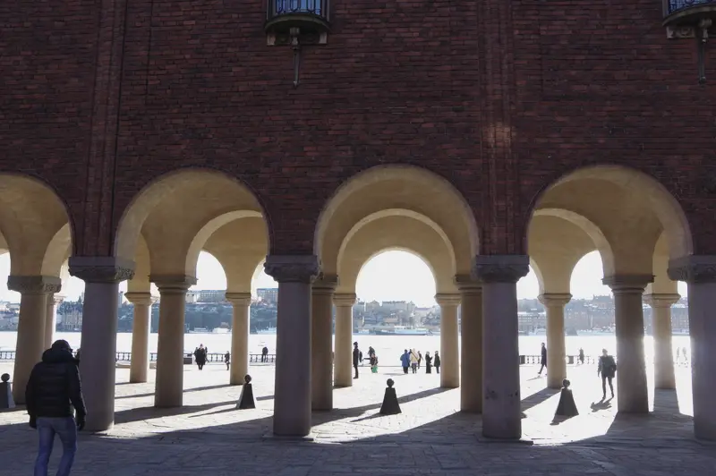 The arcade at Stockholm City Hall, a single figure under the arches and the water beyond.